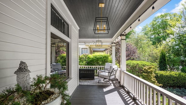 A covered porch with a wooden deck, a white railing, and a seating area with two chairs.