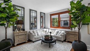 A corner living room with a white sectional sofa, a round coffee table, and two potted plants.