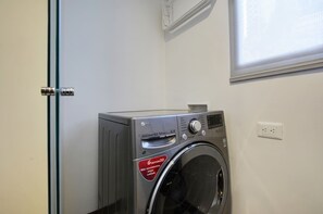 Un lave-linge compact et moderne, dans une pièce épurée et minimaliste aux murs blancs et dotée d’une fenêtre.