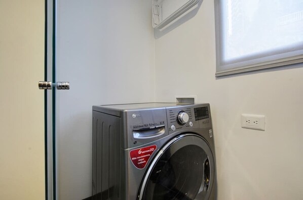A compact, modern washing machine in a clean, minimalistic room with a white wall and a window.