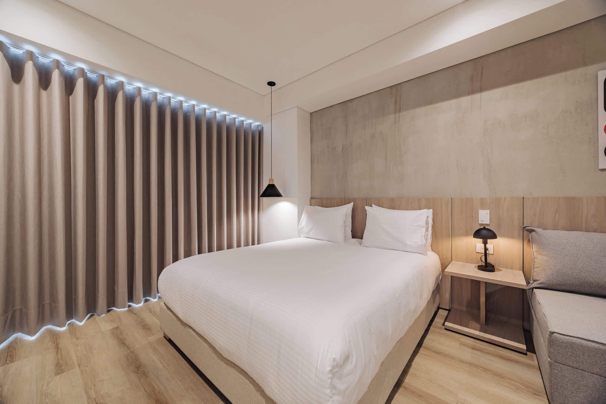 Una habitación de hotel moderna con una cama grande, una mesita de noche con lámpara y un cabecero de madera.