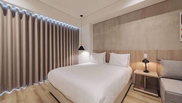 Una habitación de hotel moderna con una cama grande, una mesita de noche con lámpara y un cabecero de madera.