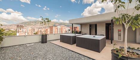 A rooftop terrace with a seating area, a small tree, and a view of the cityscape.