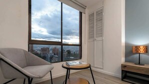 Une chambre moderne avec une grande fenêtre, une chaise, une petite table ronde et une lampe.