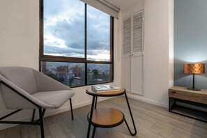 Une chambre moderne avec une grande fenêtre, une chaise, une petite table ronde et une lampe.