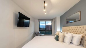 Une chambre moderne avec un grand lit, un téléviseur à écran plat, une fenêtre donnant sur la ville et une tête de lit capitonnée.