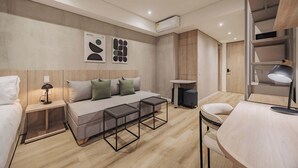 A modern hotel room with a sofa bed, a small table, a desk, and a chair. There is a wardrobe with a mirror, a lamp, and artwork on the wall. - Quadrato | Laureles Studio, w/AC, Balcony, WIFI (Medellín)