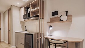 A modern kitchen with a built-in dishwasher, a microwave, and a coffee maker on the countertop. There is a small desk with a chair and a desk lamp.