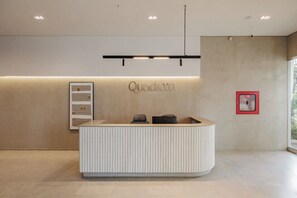 A reception desk with a modern design, a wall-mounted sign reading "Quadrato", and a framed artwork to the left. - Quadrato | Laureles Studio, w/AC, Balcony, WIFI (Medellín)