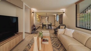 Ein modernes Wohnzimmer mit Fernseher, einer Couch, einem Couchtisch und einem Essbereich im Hintergrund.