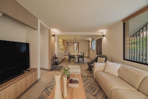 A modern living room with a TV, sofa, coffee table, and dining area in the background. - EP| Revellion 5BR Apt A/C, WorkSpace, Washer&Dryer (Medellín)