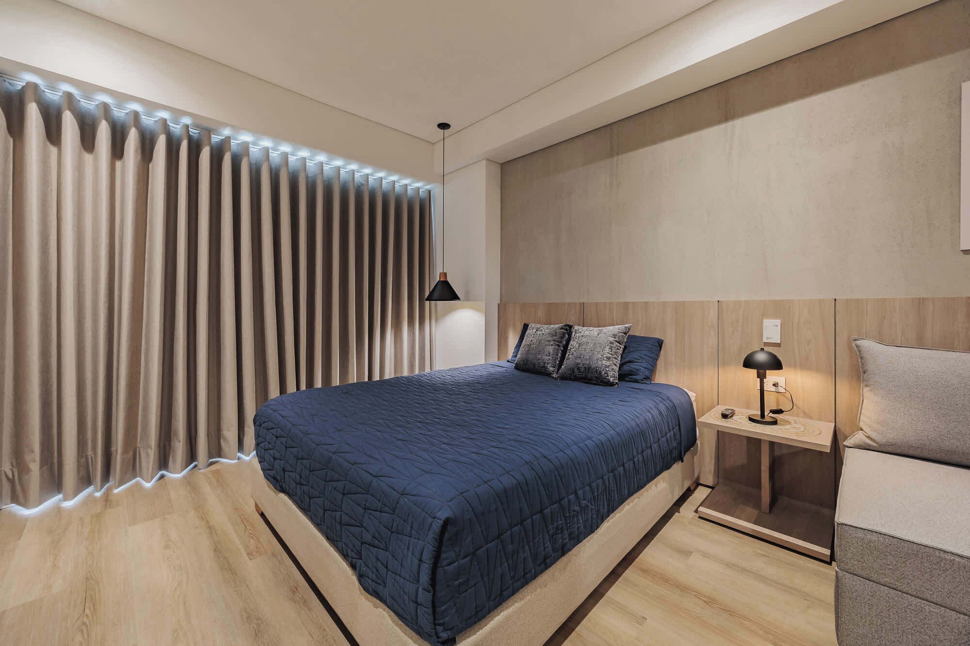 Une chambre moderne avec un grand lit, une table de chevet avec une lampe et un rideau dont le bord est illuminé.