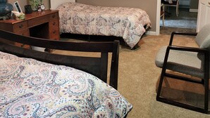 Ein Schlafzimmer mit zwei Betten, einem Schreibtisch, einem Stuhl und einer kleinen Küche im Hintergrund.