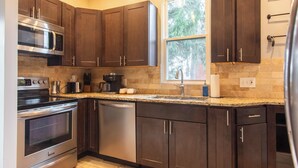 Una cocina moderna con armarios de madera oscura, electrodomésticos de acero inoxidable, una encimera de granito y una ventana con vistas a la vegetación.
