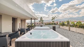 Terraza en la azotea con dos jacuzzis, mobiliario exterior y vistas a la ciudad.
