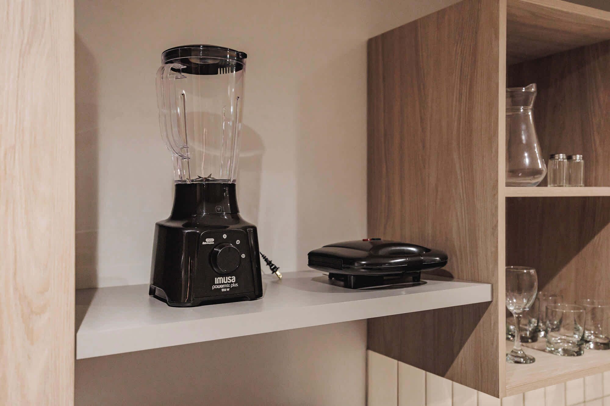 A kitchen with a black blender on a white shelf, a coffee maker, and various glassware.
