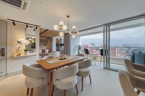 Un salon moderne avec une table à manger en bois, des chaises blanches et une grande fenêtre donnant sur la ville.