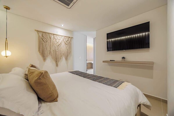 Une chambre avec un lit, un téléviseur fixé au mur et une décoration murale en macramé.