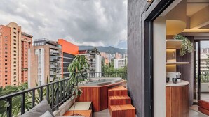 A balcony with a hot tub, wooden seating, and a view of city buildings.