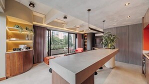 A modern kitchen with a central island, built-in shelves, and a large window offering a city view.