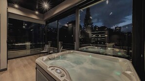 A modern spa area with a hot tub, large windows, and a city view at night.
