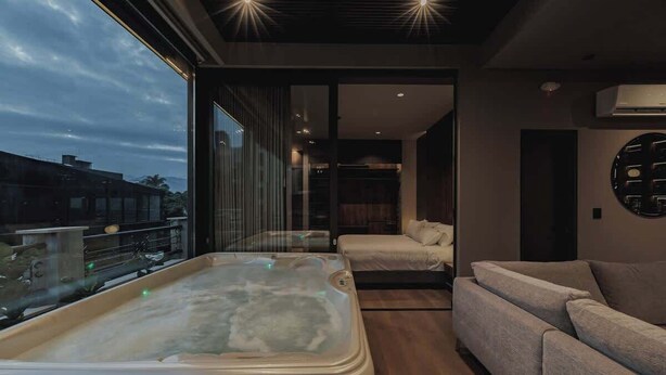 A modern room with a large window, a hot tub, a sofa, and a wall-mounted air conditioning unit.