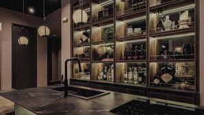 A modern bar area with a central sink, shelves with bottles, and a hanging light fixture.