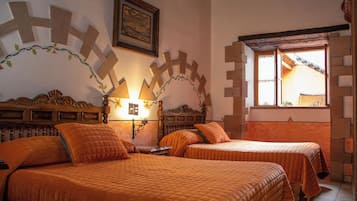 A room with two beds, a wooden headboard, a wall-mounted lamp, and a window with a view of a building.