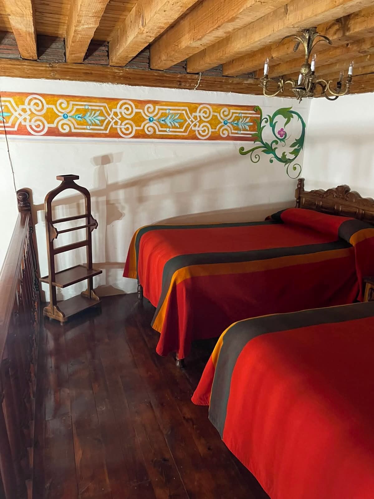 Une chambre avec deux lits, des poutres apparentes, un lustre et un panneau décoratif au mur.