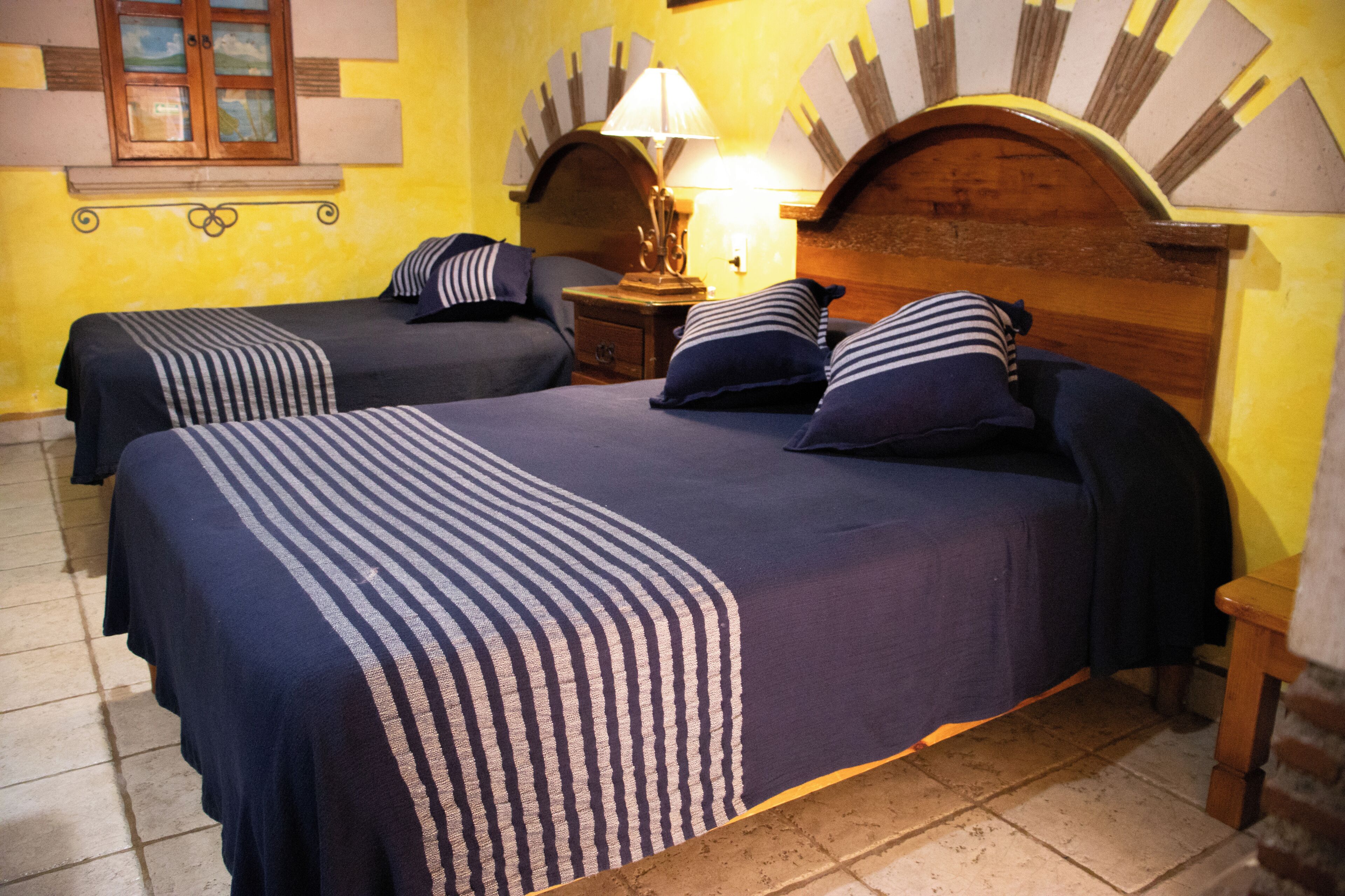 Una habitación con dos camas, una mesita de noche con lámpara, cabecero de madera y ventana con vistas.