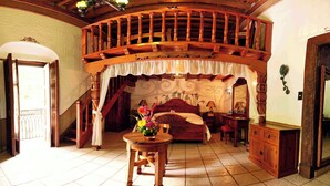 Un dormitorio con escaleras de madera, una cama con cabecera floral, una mesita de noche y una mesa con un florero.