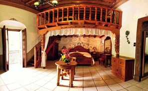 Un dormitorio con escaleras de madera, una cama con cabecera floral, una mesita de noche y una mesa con un florero.