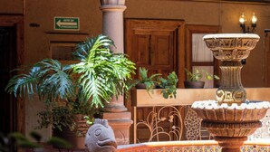 Un patio con una fuente, plantas en macetas, una escultura de piedra con forma de pez y un muro de azulejos.