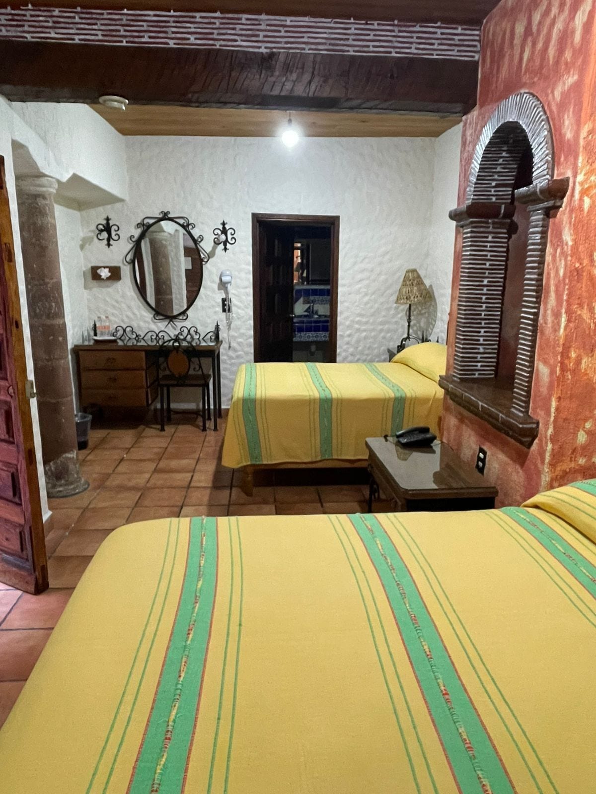 Un dormitorio con dos camas, un escritorio, un espejo y una puerta que da a otra habitación.