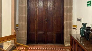 Una habitación con una puerta grande de madera, una silla de madera, piso de baldosas y un mueble con jarrones.