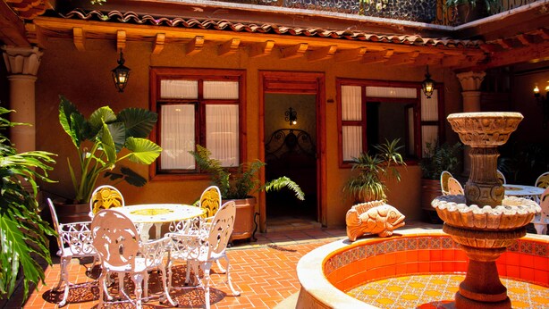 Un patio con una fuente, plantas en macetas y mobiliario exterior.