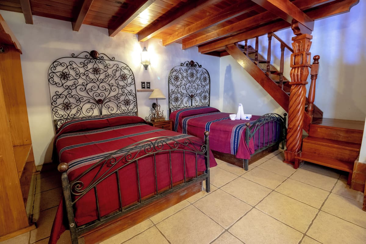 Un dormitorio con dos camas, escalera de madera y un candelabro.