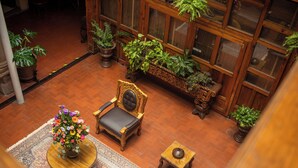 Una habitación con techos altos, un banco de madera, una silla, una mesita y plantas en macetas.