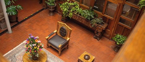 A high-ceilinged room with a wooden bench, a chair, a small table, and potted plants.