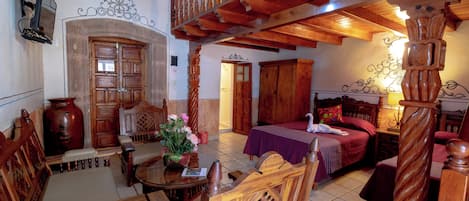 Ein traditionell eingerichteter Raum mit einem hölzernen Bett, einem Esstisch, Stühlen, einem Holzschrank und einer Treppe.