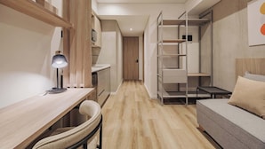 Un ambiente compatto con pavimento in legno, una scrivania con lampada, un divano e scaffalature integrate.