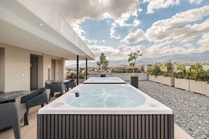 Eine Dachterrasse mit zwei Whirlpools, Sitzgelegenheiten im Freien und Blick auf die Stadt.