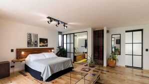 A modern bedroom with a large bed, bedside tables, a nightstand, a wooden floor, and a large window.