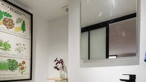 A modern bathroom with a white toilet, a wooden vanity with a white sink, and a framed botanical illustration on the wall.