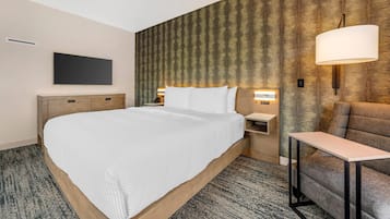 Quarto de hotel com uma cama grande, uma mesa de cabeceira, um abajur e um sofá.