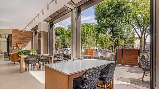 Un espace de restauration extérieur moderne, doté d’un îlot central et de chaises en osier noir.