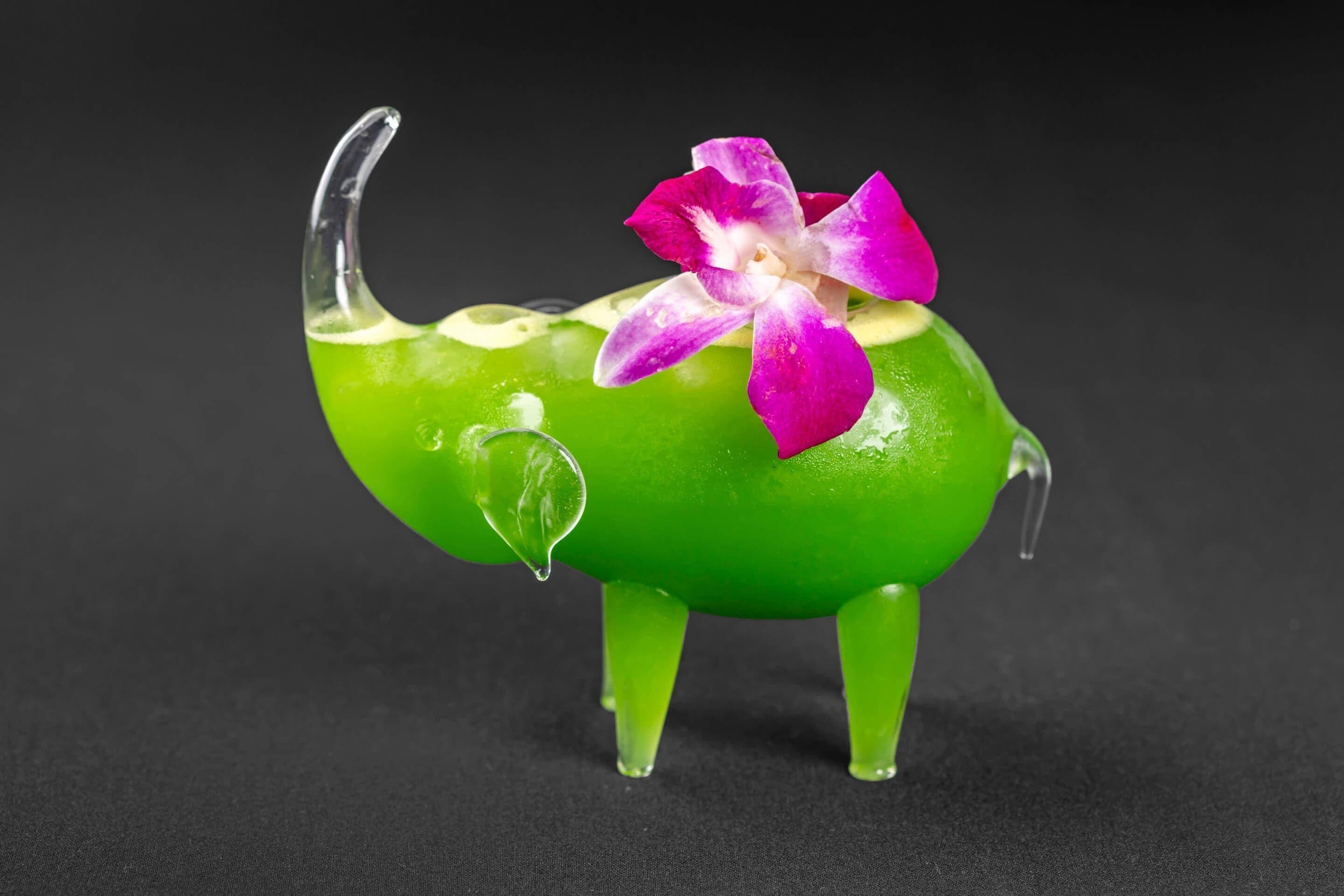 A green glass elephant with a pink flower on its back.