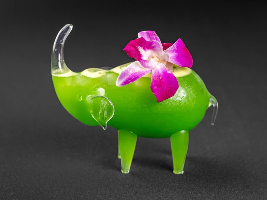 A green glass elephant with a pink flower on its back.