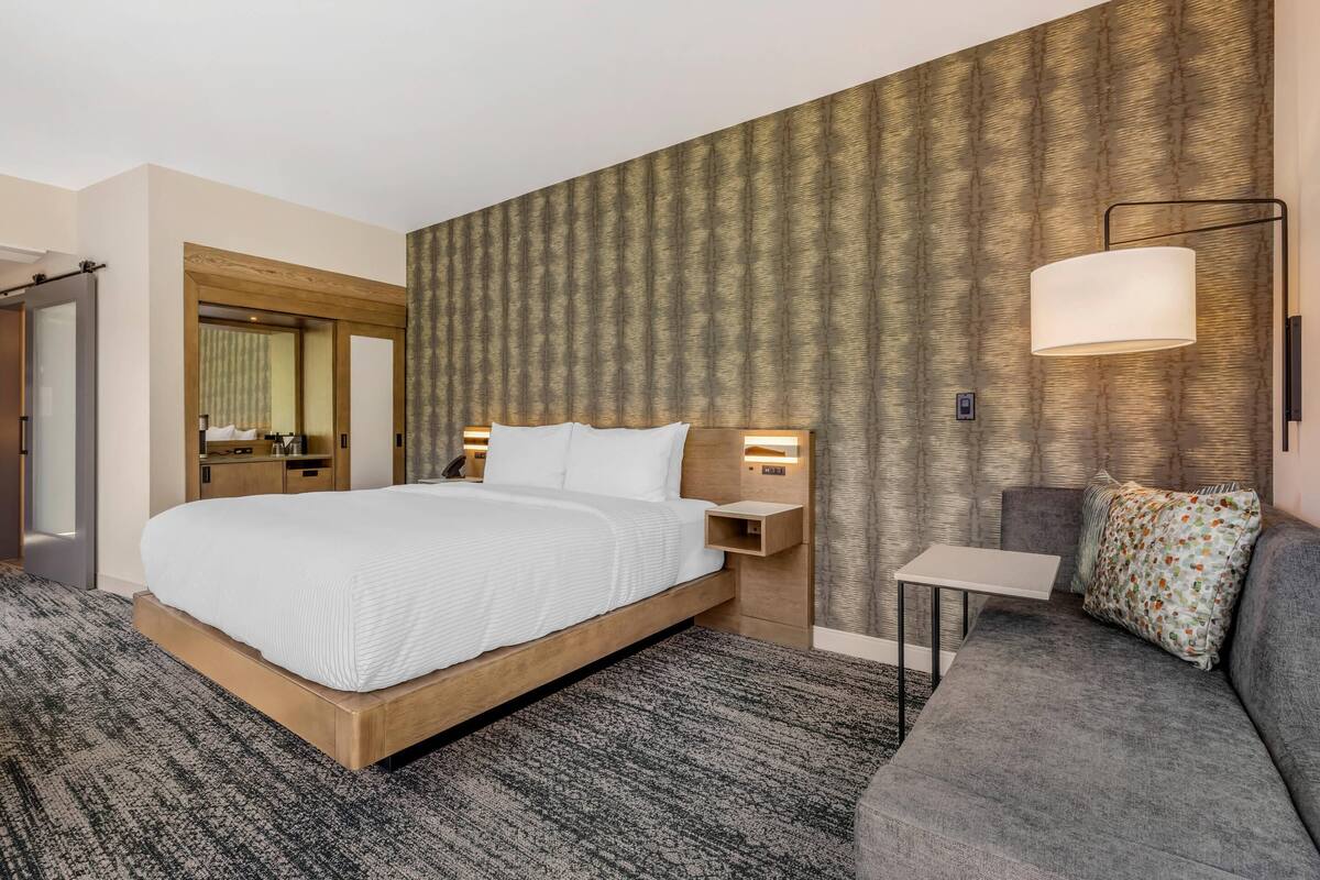 Une chambre d’hôtel avec un grand lit, un canapé, une petite table, une lampe fixée au mur et un miroir.