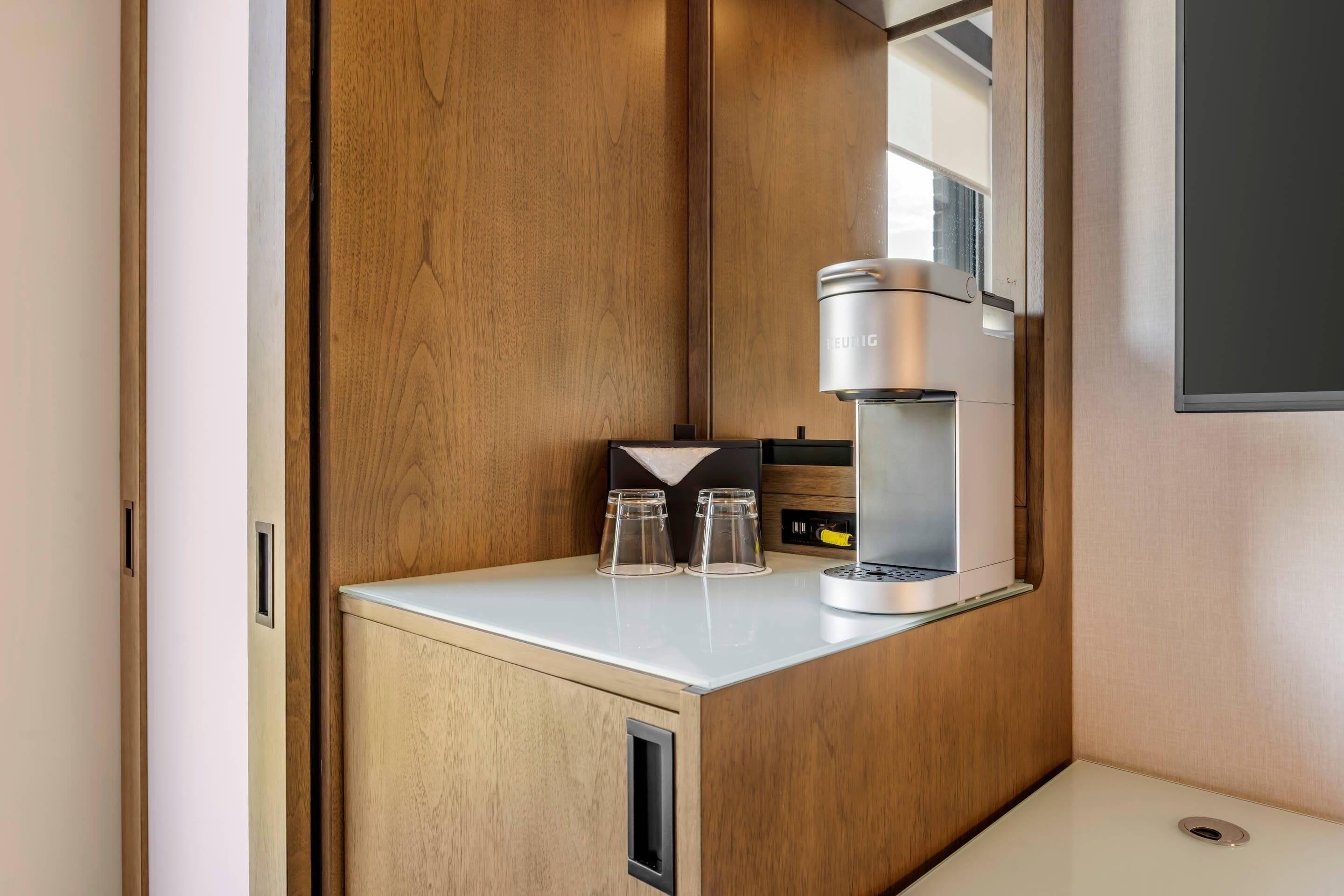 A compact kitchenette with a built-in coffee maker, two glasses, and a small cabinet.